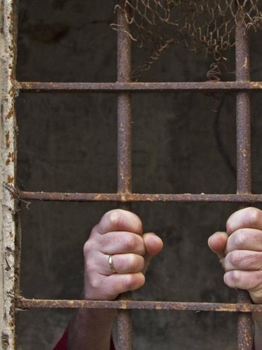 Die Hände eines Gefangenen an einem Gitterfenster.