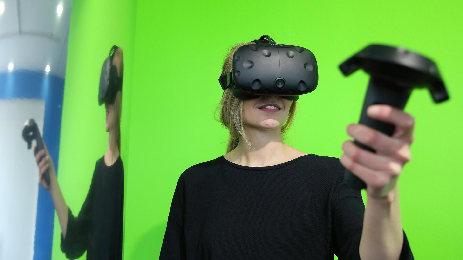 Eine Frau steht am 23.05.2017 im NRW-Forum in Düsseldorf vor einem grünem Hintergrund. Sie trägt eine Virtual-Reality-Brille und hält einen PC Controller, mit dem sie ihre virtuelle-Welt und Erlebnis steuert. Foto: David Young / dpa