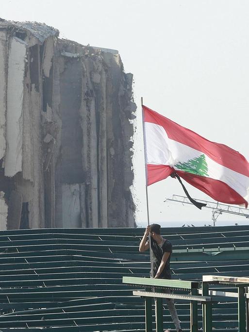 Vor der Kulisse des zerstörten Beiruts hält ein Demonstrant eine libanesische Flagge.