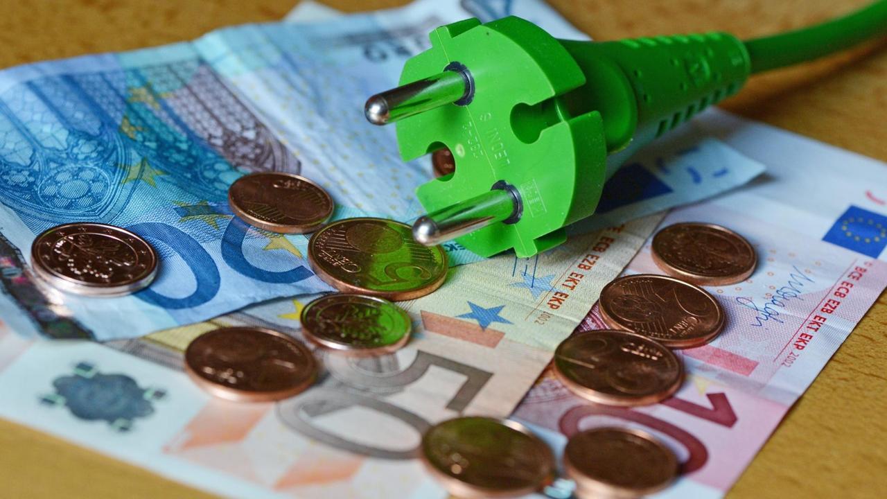 Ein grünes Stromkabel mit einem grünen Stromstecker liegt auf Euro Geldscheinen und Centmünzen.