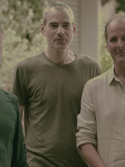 Drei Männer stehen für ein Porträt zusammen im Grünen