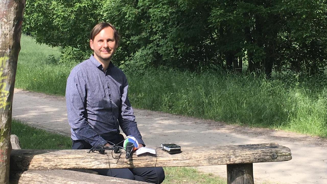 Stefan Ziller. Ein Mann sitzt auf einer Holzbank in einem Park.