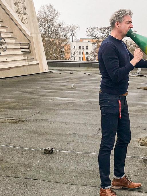 André Nicke steht auf dem Dach der Uckermärkischen Bühnen Schwedt und hält ein Magaphon in der Hand.