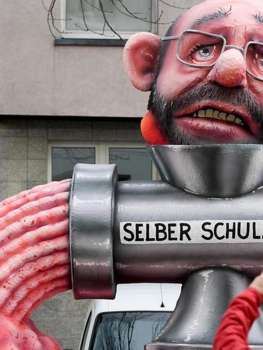 12.02.2018, Nordrhein-Westfalen, Düsseldorf: Ein politischer Mottowagen mit der Figur von "Martin Schulz, dem noch Vorsitzenden der SPD" nimmt an dem Rosenmontagszug teil. Ein Zuschauer fotografiert den Mottowagen.