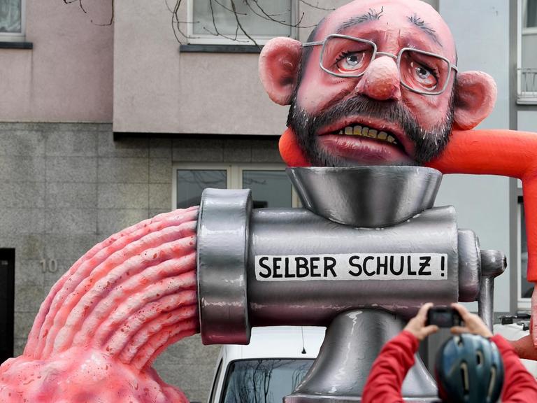12.02.2018, Nordrhein-Westfalen, Düsseldorf: Ein politischer Mottowagen mit der Figur von "Martin Schulz, dem noch Vorsitzenden der SPD" nimmt an dem Rosenmontagszug teil. Ein Zuschauer fotografiert den Mottowagen.
