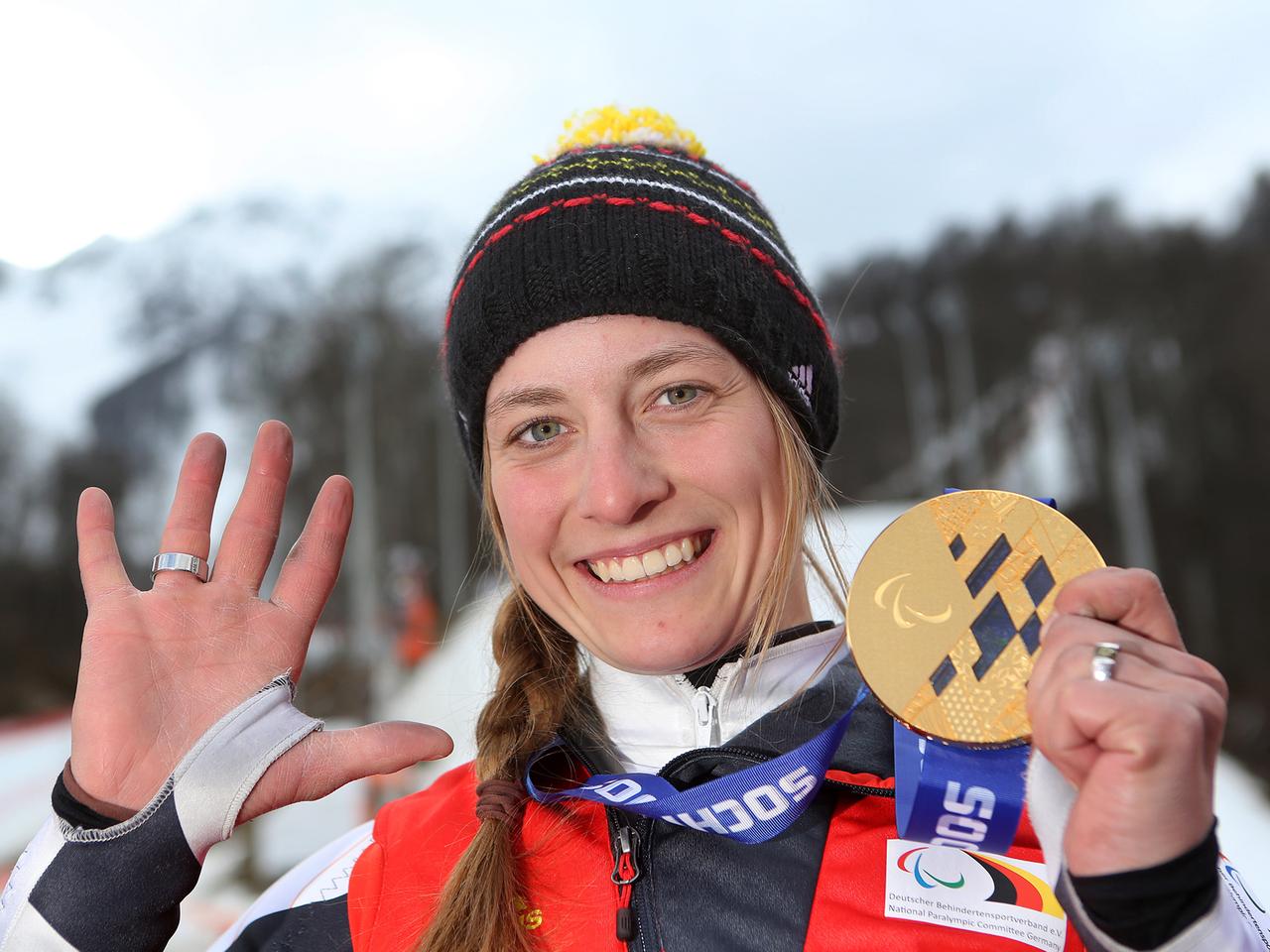 Die deutsche Mono-Ski-Fahrerin Anna Schaffelhuber hält ihre fünfte Goldmedaille bei den Paralympics in Sotschi strahlend in die Höhe und zeigt mit der anderen Hand die Zahl Fünf an.