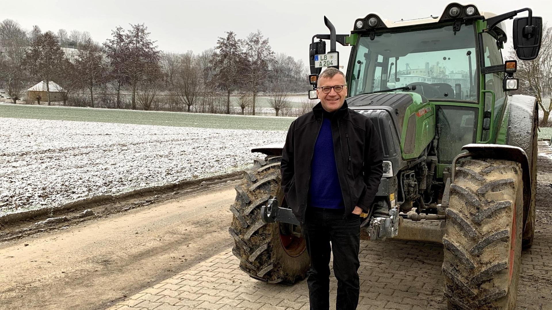 Marcus Arzt ist Ökobauer in Ditzingen und Biolandchef in Baden-Württemberg. Er steht neben seinem schneebedecktem Acker und grünem Traktor im Winter.