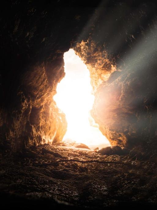 Eingang einer einsamen Höhle, Aufnahme aus dem Inneren. Ein heller Lichtstrahl strömt hinein.
