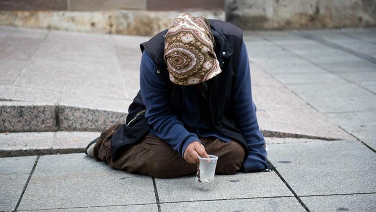 Eine Bettlerin in Berlin sitzt mit gesengtem Haupt auf der Straße.