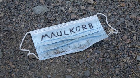 Auf einem Mundschutz steht der Schriftzug Maulkorb.