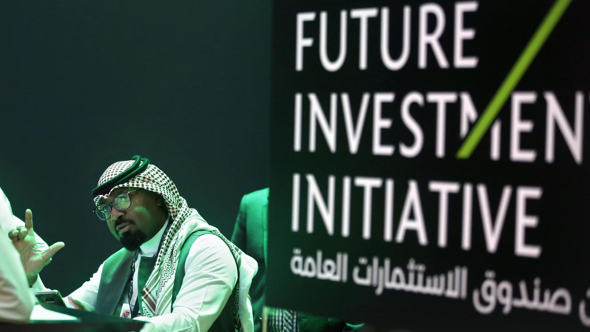 Ein Mitarbeiter der Investorenkonferenz in Riad druckt Unterlagen für die Teilnehmer aus, rechts sieht man den Schriftzug der Konferenz "Future Investment Initiative".