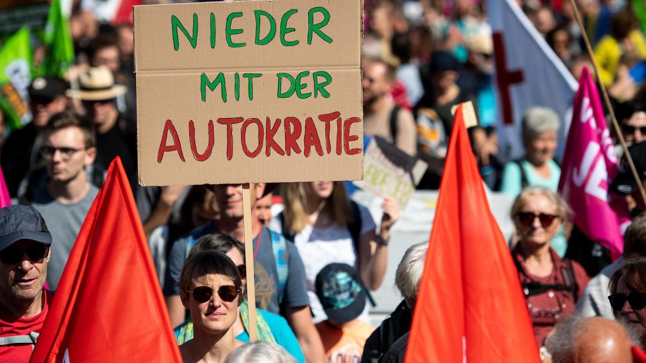 Ein Frau demonstriert mit einem Schild mit der Aufschrift "Nieder mit der Autokratie".
