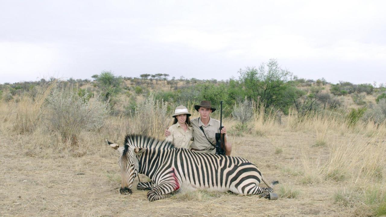 Junge Jägerin und junger Jäger posieren kniend mit Gewehr hinter einem erschossenen Zebra.