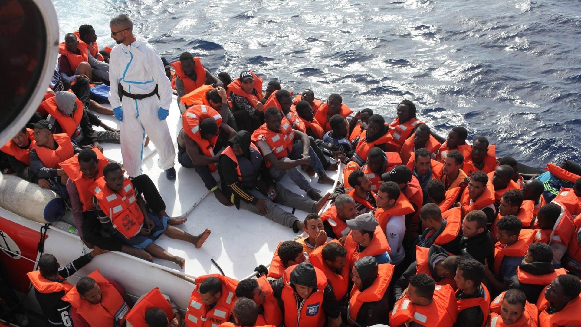 Viele Flüchtlinge sitzen mit Rettungs-Westen in einem Boot.