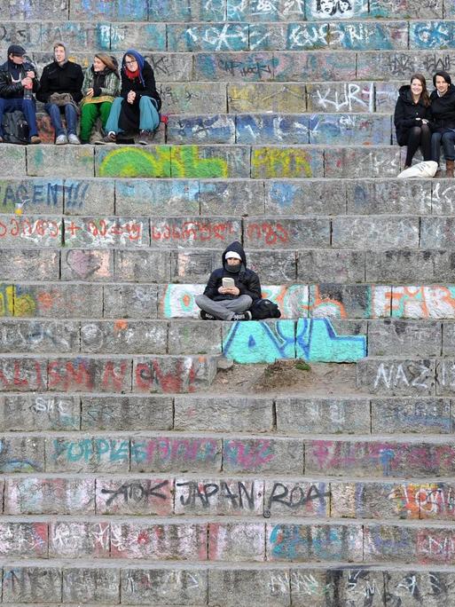 Menschen sitzen auf den Stufen des kleinen Amphitheaters im Mauerpark in Berlin. Der Park im ehemaligen Grenzgebiet zwischen beiden Berliner Stadthälften ist ein beliebter Treffpunkt.
