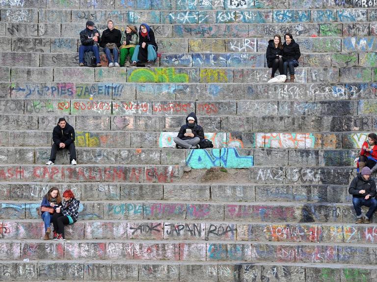 Menschen sitzen auf den Stufen des kleinen Amphitheaters im Mauerpark in Berlin. Der Park im ehemaligen Grenzgebiet zwischen beiden Berliner Stadthälften ist ein beliebter Treffpunkt.