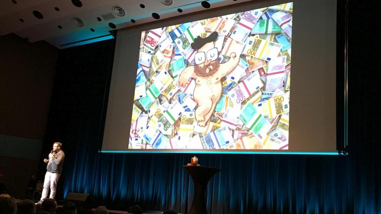 Eine Folie aus dem Vortrag von Johannes Kretzschmar zeigt eine Comiczeichnung von ihm selbst, wie er auf einem Haufen Geldscheine liegt.