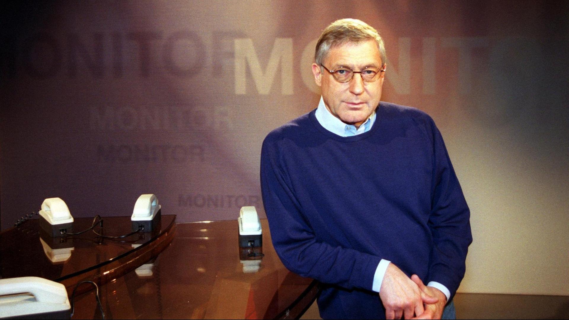 Ein Mann in Hemd und blauem Pullover steht in einer altmodischen Fernsehstudiokulisse: Es ist der damalige Redaktionsleiter des WDR-Politmagazins "Monitor": Klaus Bednarz.