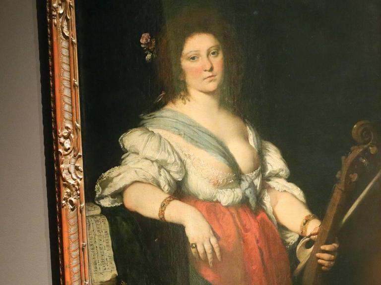 Gemälde "Die Gambenspielerin" von Bernarndo Strozzi. Sie hält eine Gambe und einen Bogen in der linken Hand, sie trägt ein rot-weißes Mieder-Kleid mit einem tiefen Ausschnitt, ihre linke Brust ist nahezu ganz entblößt