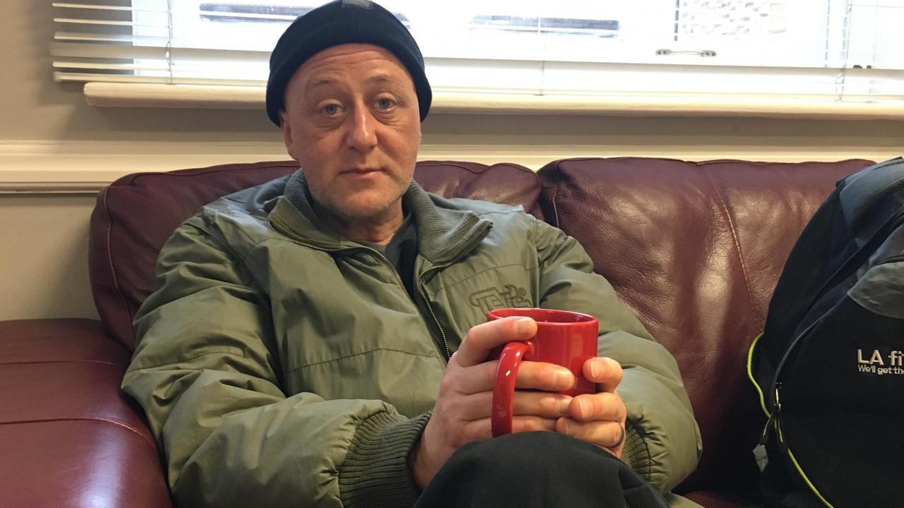 Der ehemalige Obdachlose Martin sitzt auf der Couch im Windsor Homeless Project und hält eine Tasse in der Hand