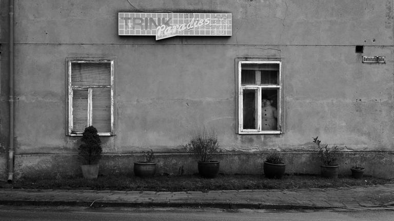 Im Erdgeschoßfester einer Hausfassade, mit dem Schild "Trink Paradies", steht eine Schneemannfigur.