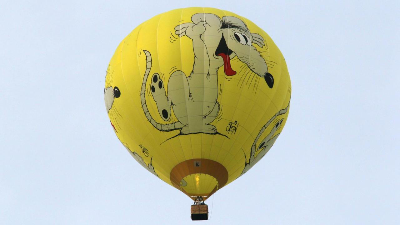 Ein gelber Heißluftballon mit einer von Uli Stein gezeichneten Maus am Himmel.