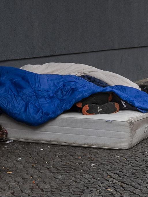 Berlin: Zwei Obdachlose liegen an einer Hauswand auf einer Matratze und schlafen.