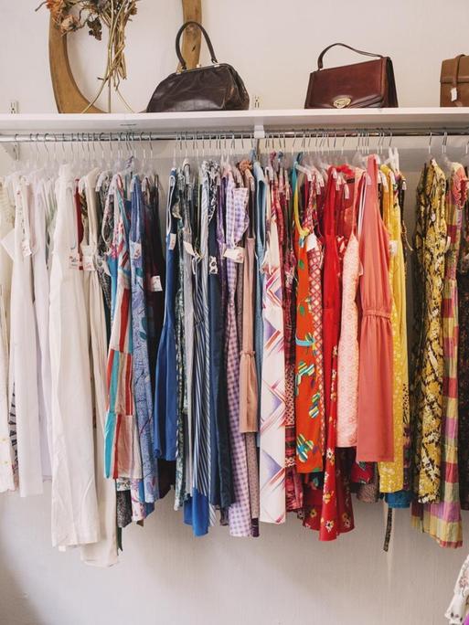 In einem Geschäft steht eine Kleiderstange bestückt mit farbenfroher Kleidung.