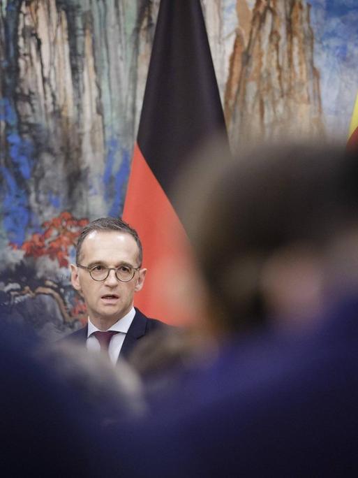 Bundesaußenminister Heiko Maas (SPD) vor der deutschen und der chinesischen Flagge - im Vordergrund sind Rücken von Zuhörenden zu sehen, aufgenommen im November 2018
