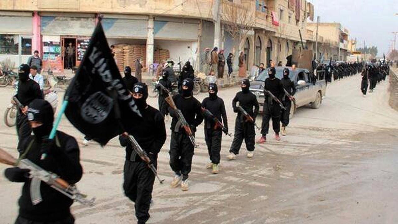Ein Propagandabild der Terrormiliz IS: Mitglieder in schwarzen Overalls und mit Gewehren in der Hand marschieren durch Raqqa in Syrien. Der erste Mann trägt die schwarz IS-Fahne.