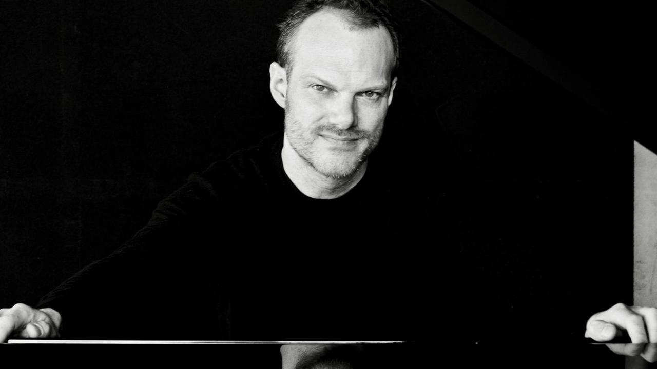 Der Pianist Lars Vogt sitzt an einem Flügel und lächelt in die Kamera.