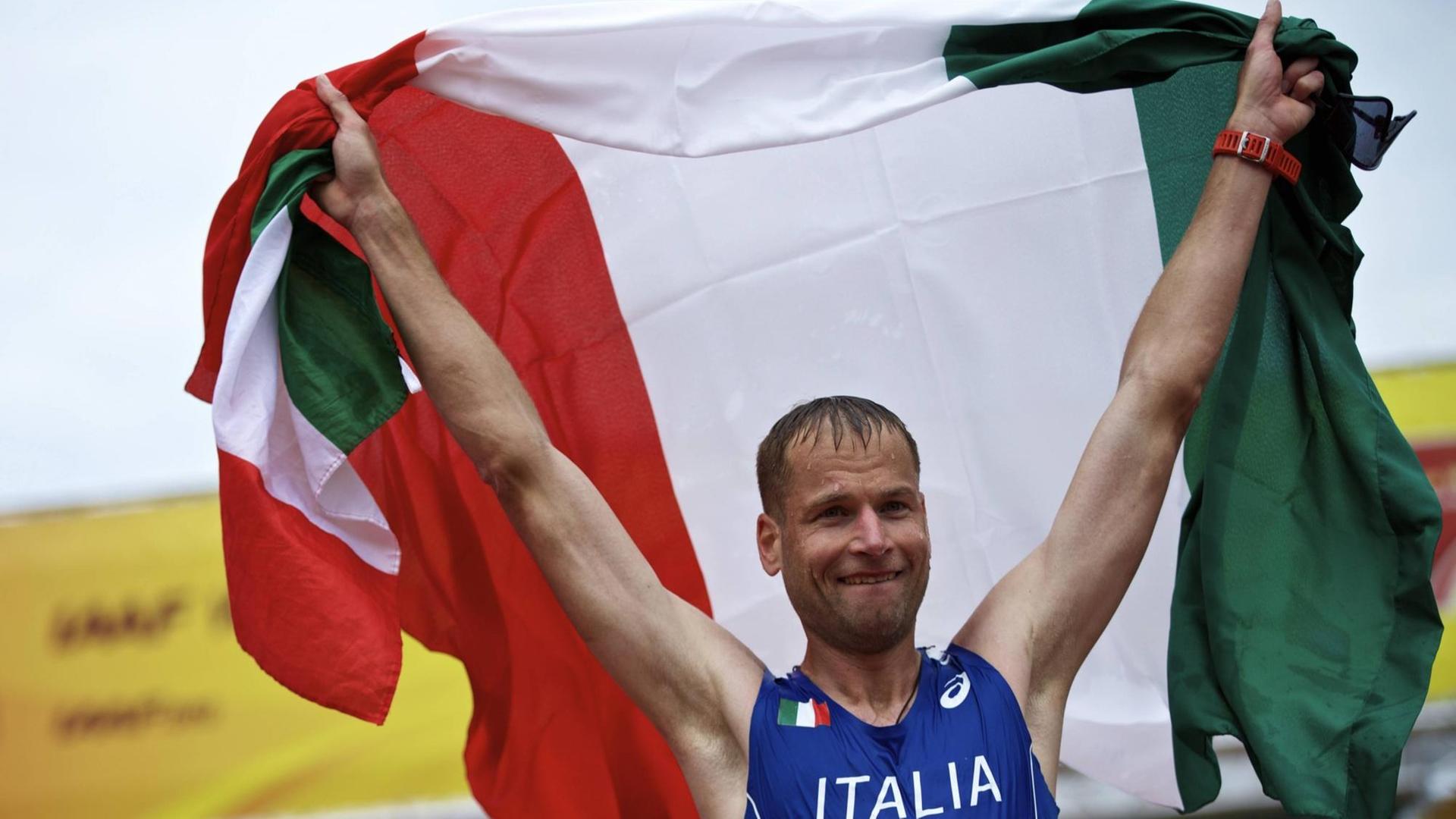 Alex Schwazer hält die italienische Fahne über seinen Kopf.