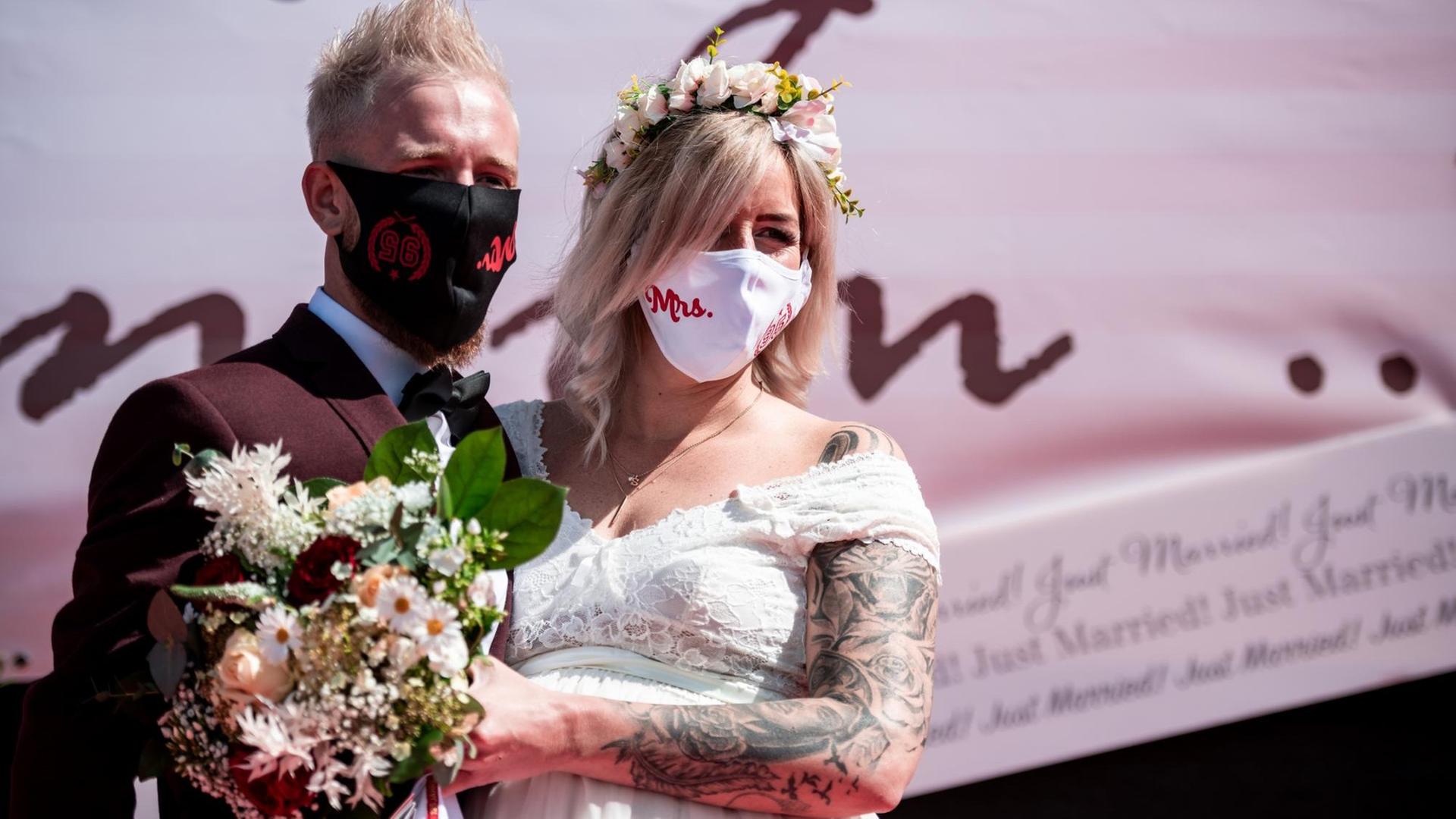 Ein Braut-Paar steht mit Mund-Schutz auf einer Bühne.