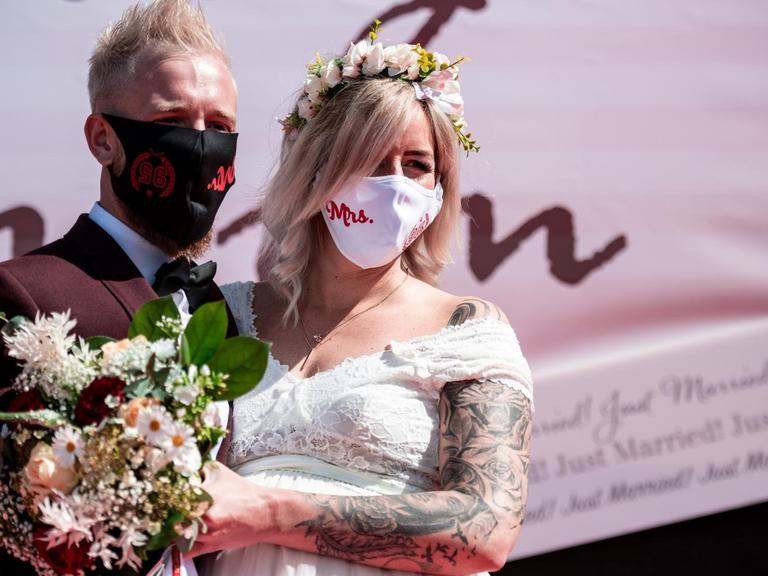 Das Brautpaar Janine und Philip Scholz steht bei der Trauung im Autokino mit Mundschutz vor der Bühne.