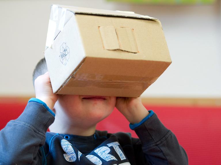 Der fünfjährige Valentino mit Down-Syndrom sitzt am 05.12.2013 während der Ergotherapie in einem Therapiezimmer des Sozialpädiatrischen Zentrums (SPZ) im Krankenhaus Dresden-Neustadt in Dresden (Sachsen) und hält ein Haus aus Pappe vor sein Gesicht.