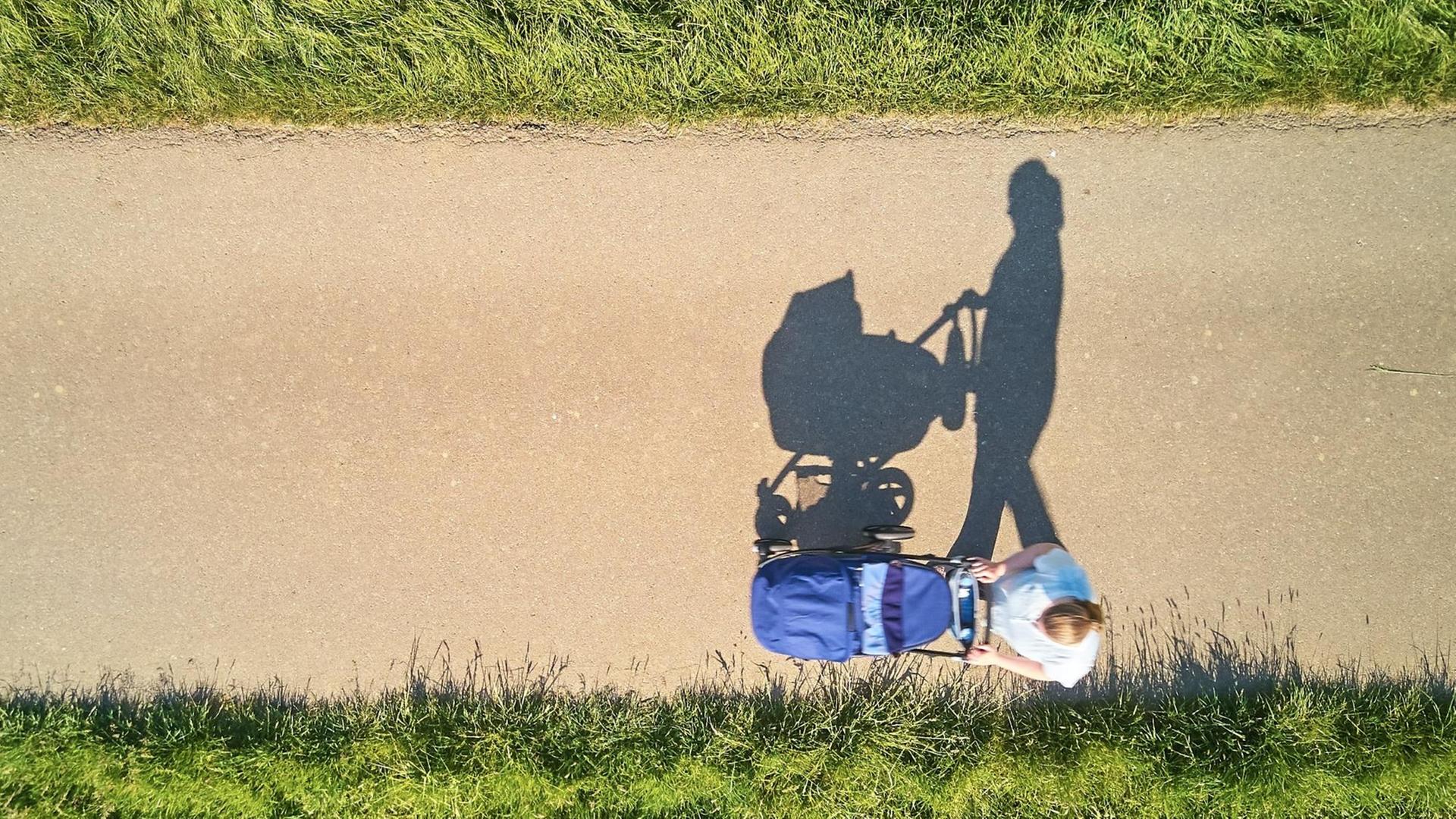 Luftbild: Eine Mutter mit Kinderwagen auf einsamer Straße.