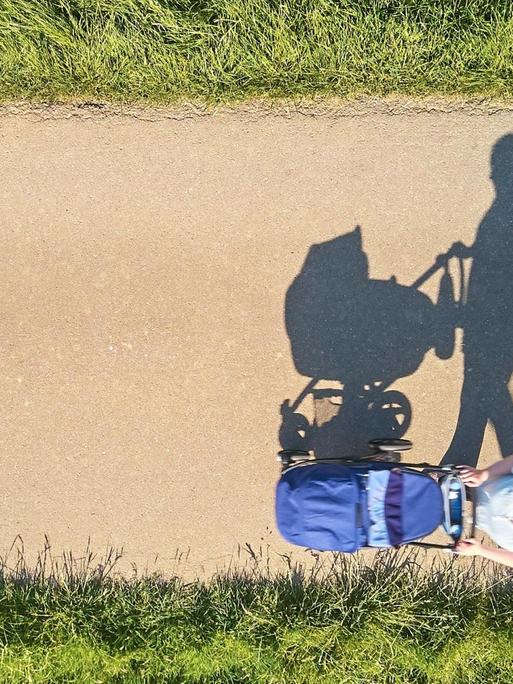 Luftbild: Eine Mutter mit Kinderwagen auf einsamer Straße.