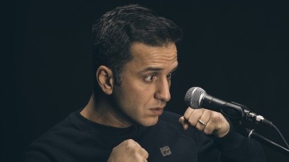 Özcan Cosar schielt auf ein vor ihm stehendes Mikrofon, dabei ballt er seine Hände zu Fäusten.