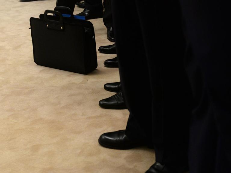 Eine Reihe von Männern in Anzügen, der Blick geht auf Hosen und Schuhe.