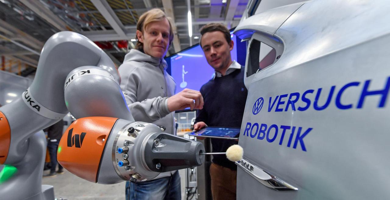 In einer Fertigungshalle des VW-Werks Zwickau stehen zwei Männer vor einem silbernen Roboter und lernen diesen über Gesten an.