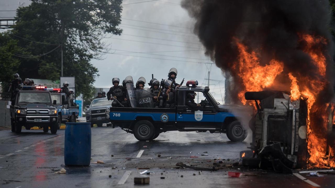 02.09.2018, Nicaragua, Managua: Schwer bewaffnete Polizisten sitzen auf einem Pick-up und stehen neben einem brennenden Polizeifahrzeug. Mindestens eine Person wurde in Managua verletzt als Unbekannte mit Schusswaffen auf die Teilnehmer einer Demonstration gegen die Regierung schossen. Foto: Carlos Herrera/dpa | Verwendung weltweit