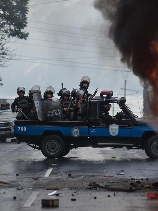 02.09.2018, Nicaragua, Managua: Schwer bewaffnete Polizisten sitzen auf einem Pick-up und stehen neben einem brennenden Polizeifahrzeug. Mindestens eine Person wurde in Managua verletzt als Unbekannte mit Schusswaffen auf die Teilnehmer einer Demonstration gegen die Regierung schossen. Foto: Carlos Herrera/dpa | Verwendung weltweit