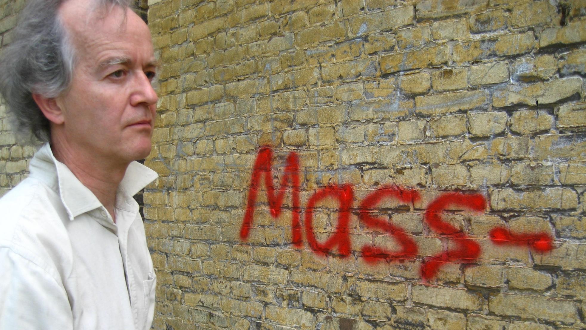 Peter Ablinger steht an einer alten Ziegelwand auf die er "Mass-" gesprayt hat