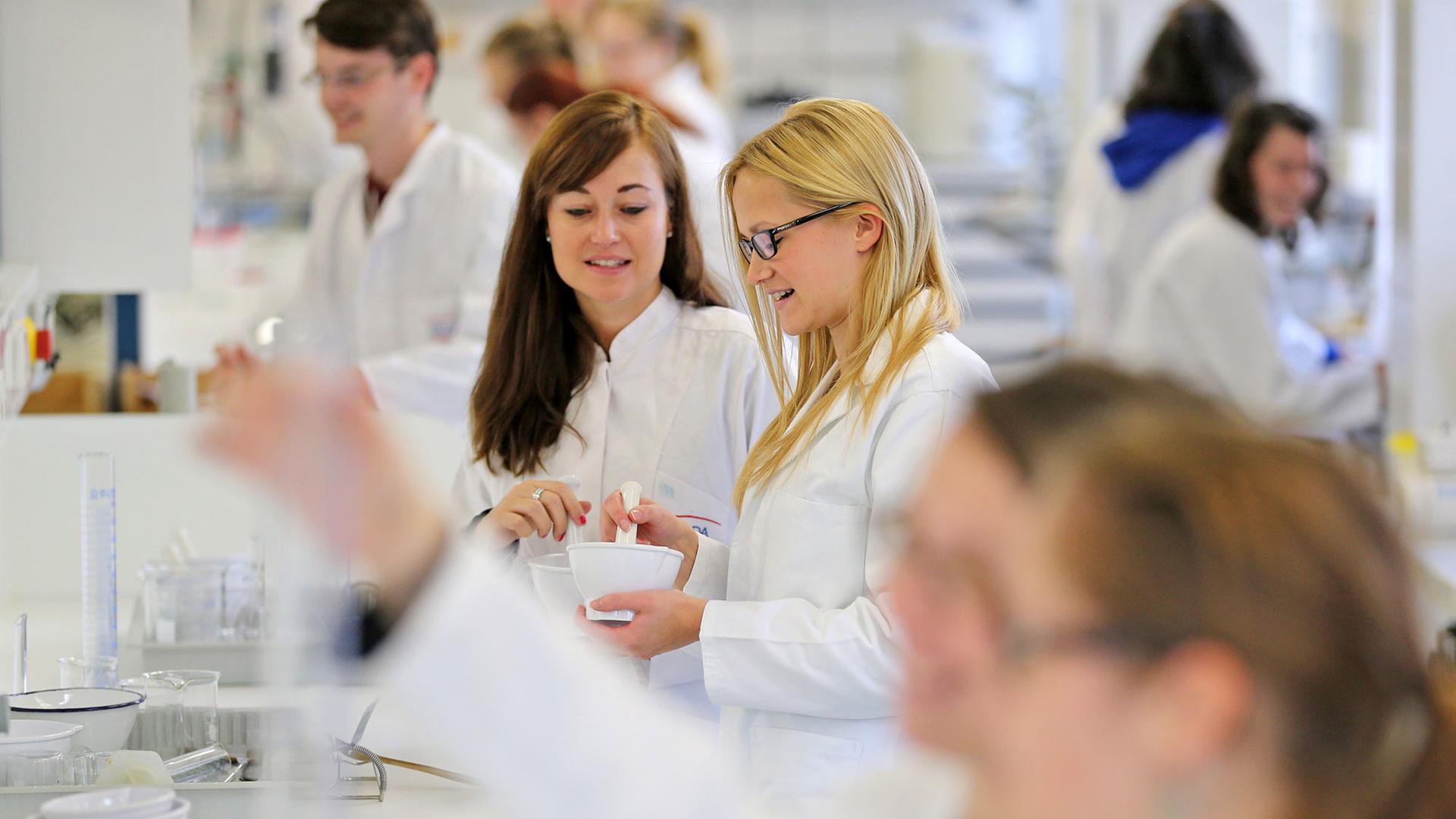Mehrere Studenten in weißen Kitteln arbeiten in einem Labor. 