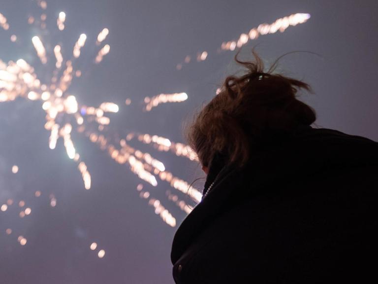 Eine Frau schaut sich ein Silvesterfeuerwerk an.