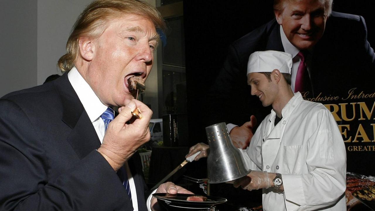 Trump isst ein Steak. Daneben ein Koch und ein Plakat mit seinem Konterfei.