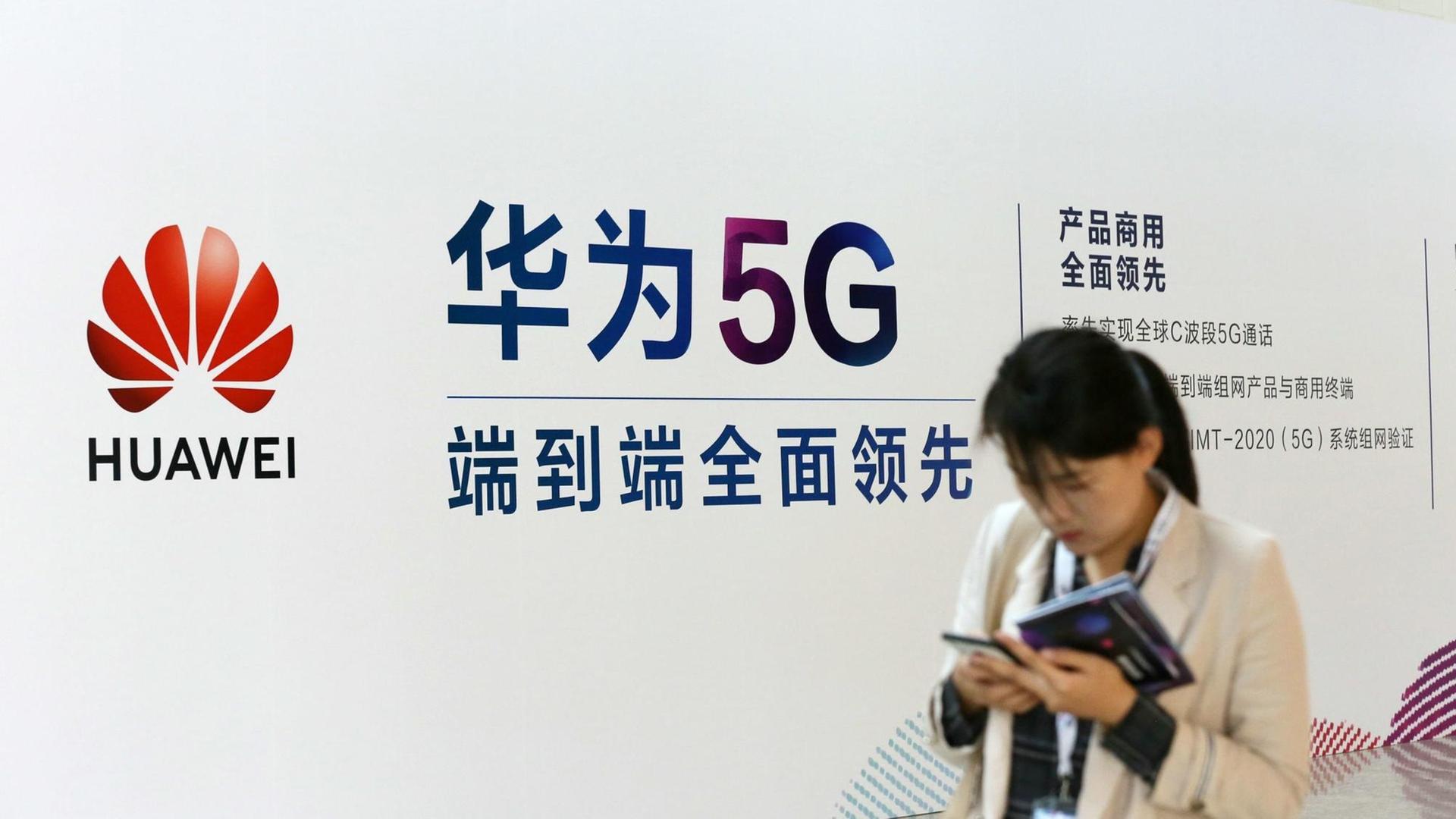 Eine Frau geht an einem Stand des chinesischen Technologiekonzerns Huawei mit Werbung für die 5G-Technik auf der Messe PT in Peking vorbei