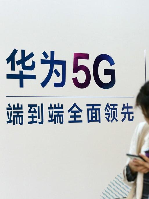 Eine Frau geht an einem Stand des chinesischen Technologiekonzerns Huawei mit Werbung für die 5G-Technik auf der Messe PT in Peking vorbei