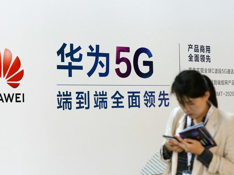 Eine Frau geht an einem Stand des chinesischen Technologiekonzerns Huawei mit Werbung für die 5G-Technik auf der Messe PT in Peking vorbei