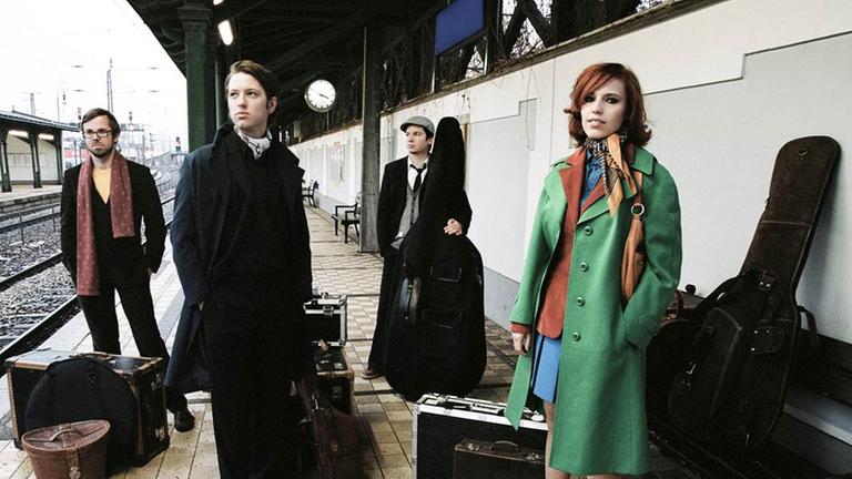 Die Mitglieder von "Falb Fiction" stehen mit ihren Instrumenten auf einem Bahnsteig.
